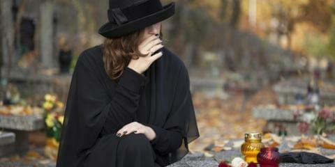 A person sitting in a cemetery in all black, mourning the loss of a loved one to a wrongful death accident.