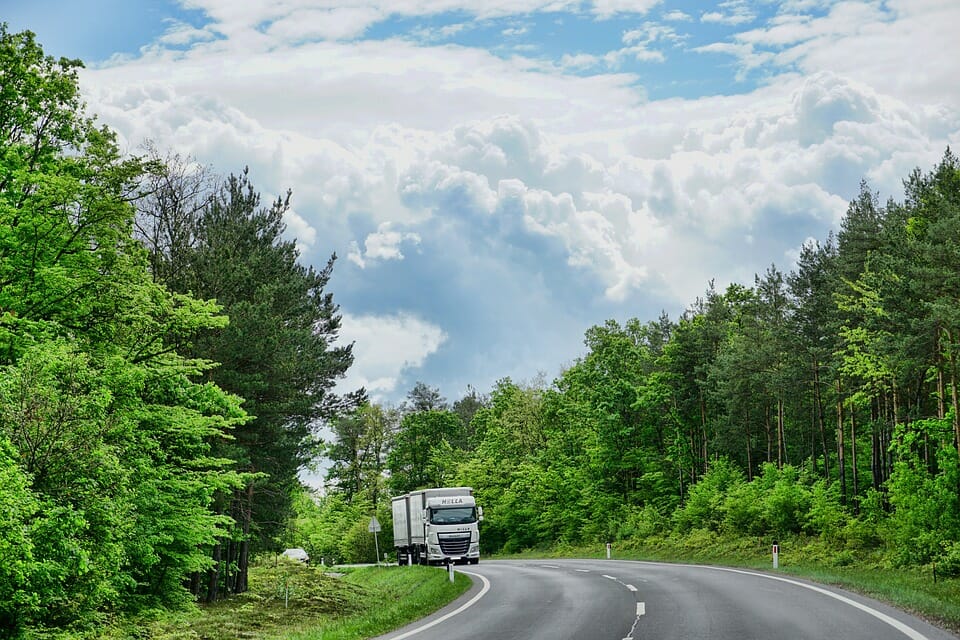 A tractor trailer traveling uphill on a two-lane road with the woods on either side.