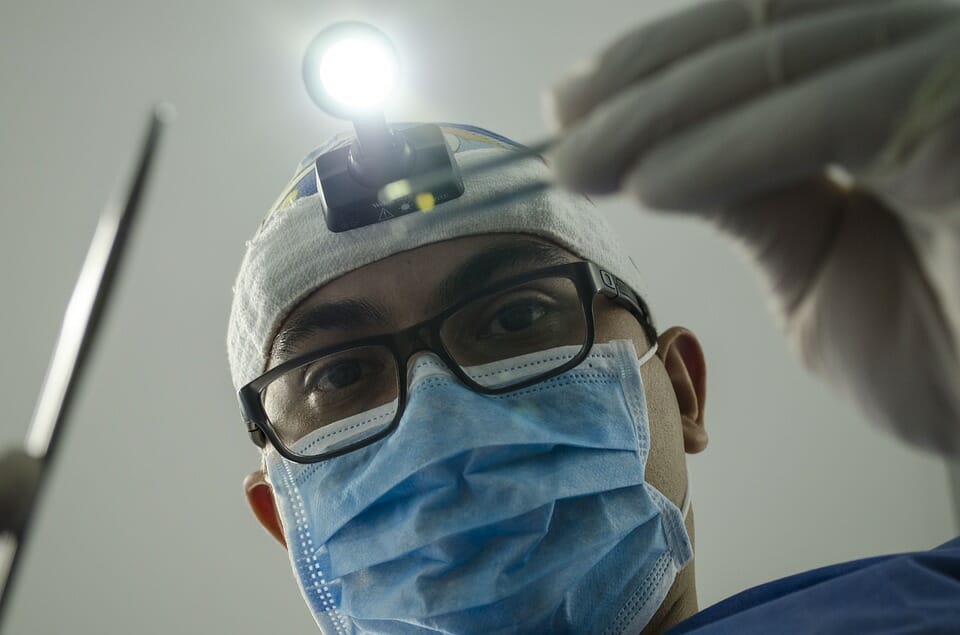 A doctor looking over the patient with their medical instruments and headlight.