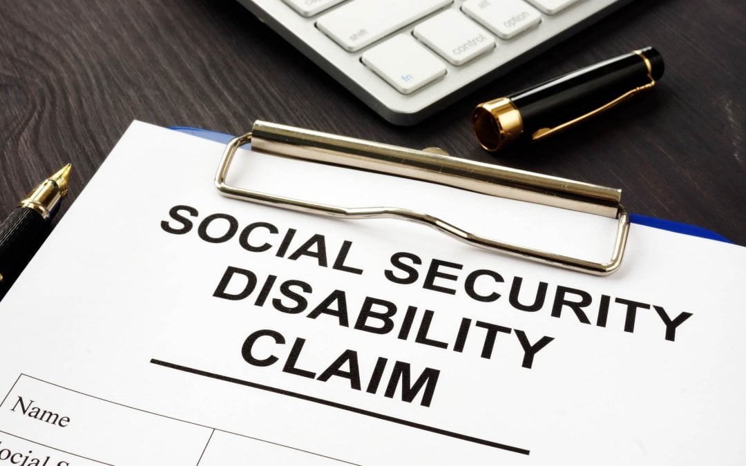 A social security disability claim application on a clipboard sitting on a desk near a computer keyboard.